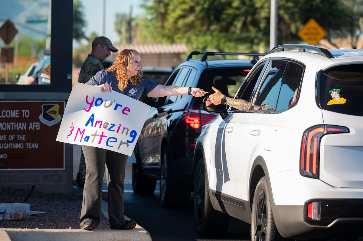 Katherine Lord, Integrated Resilience Office prevention analyst, hands a 988 Day token to a person entering Davis-Monthan Air Force Base, Arizona, Sept. 8, 2025. 988 Day highlights the importance of mental health, reminding our community that help is always just three numbers away. (U.S. Air Force photo by Airman 1st Class Samantha Melecio)