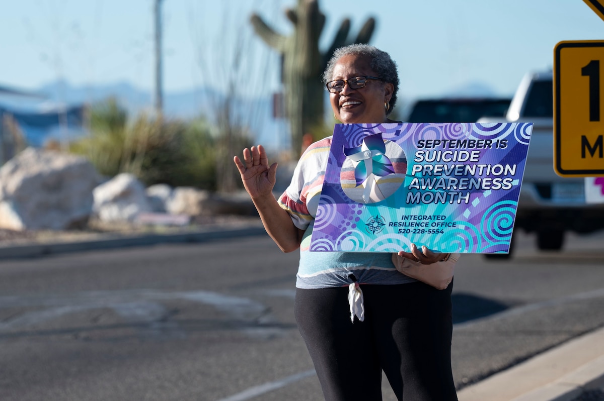 Sylvia Thomas, 355th Component Maintenance Squadron True North embedded provider, waves to drivers entering Davis-Monthan Air Force Base, Arizona, Sept. 8, 2025. Airmen and civilians greeted personnel at base entry points with messages of encouragement and tokens in recognition of 988 Day. (U.S. Air Force photo by Airman 1st Class Samantha Melecio)