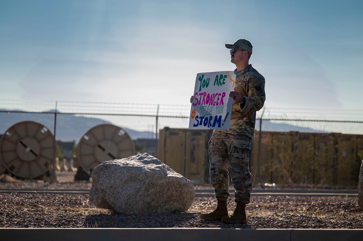 A U.S. Airman holds a sign for drivers entering Davis-Monthan Air Force Base, Arizona, Sept. 8, 2025. Members of the Desert Lightning Team gathered at installation entry control points to share encouraging messages and distribute mementos in support of suicide prevention awareness. (U.S. Air Force photo by Airman 1st Class Samantha Melecio)