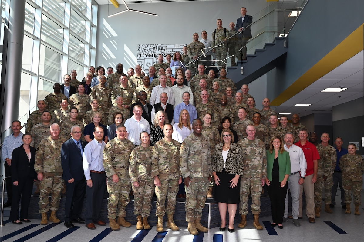 Civilian and uniformed military personnel gather for a group photo.