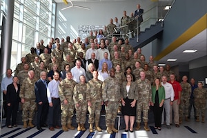 Civilian and uniformed military personnel gather for a group photo.