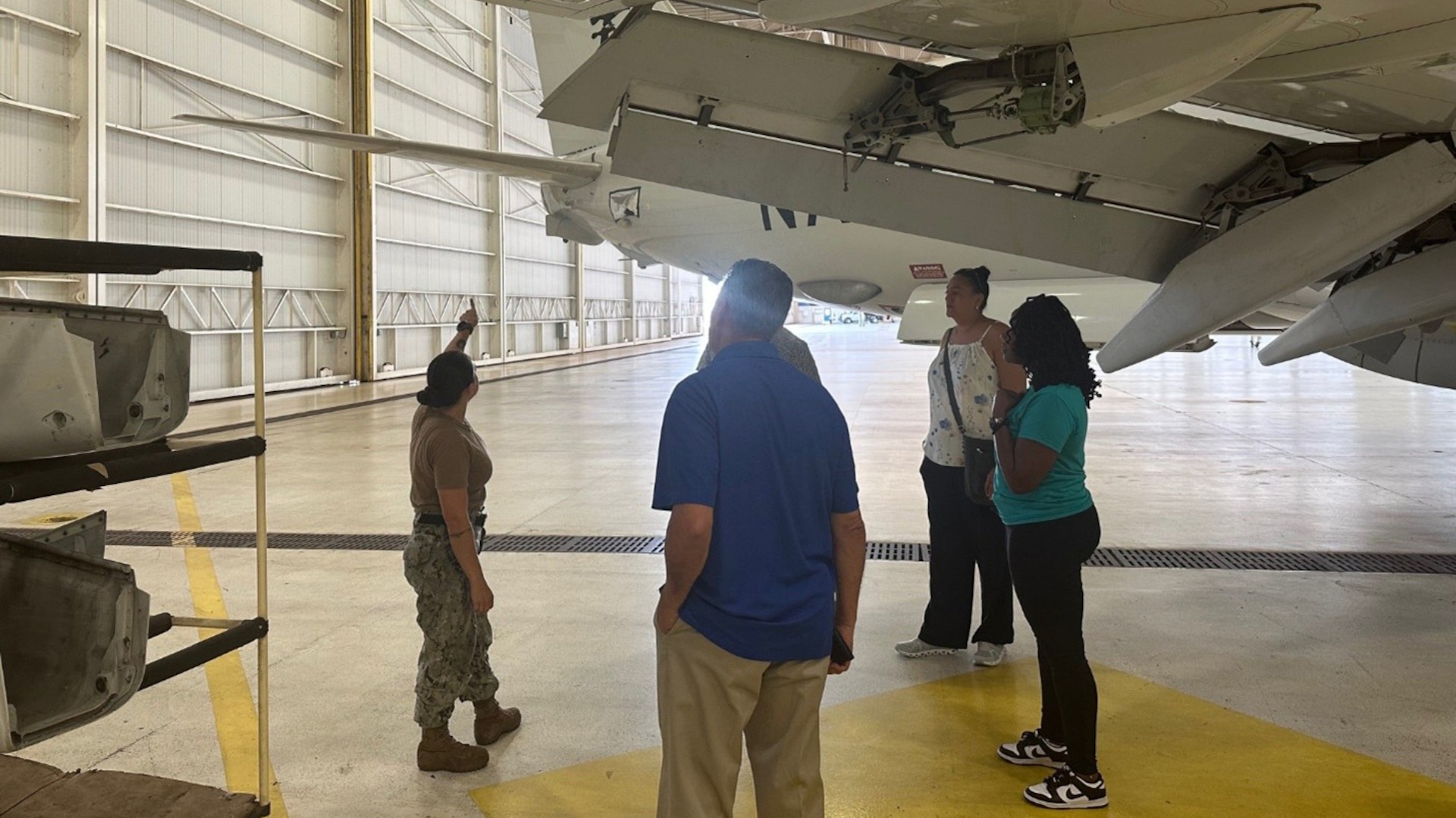 A sailor explains parts of the P-8 aircraft to three civilians.