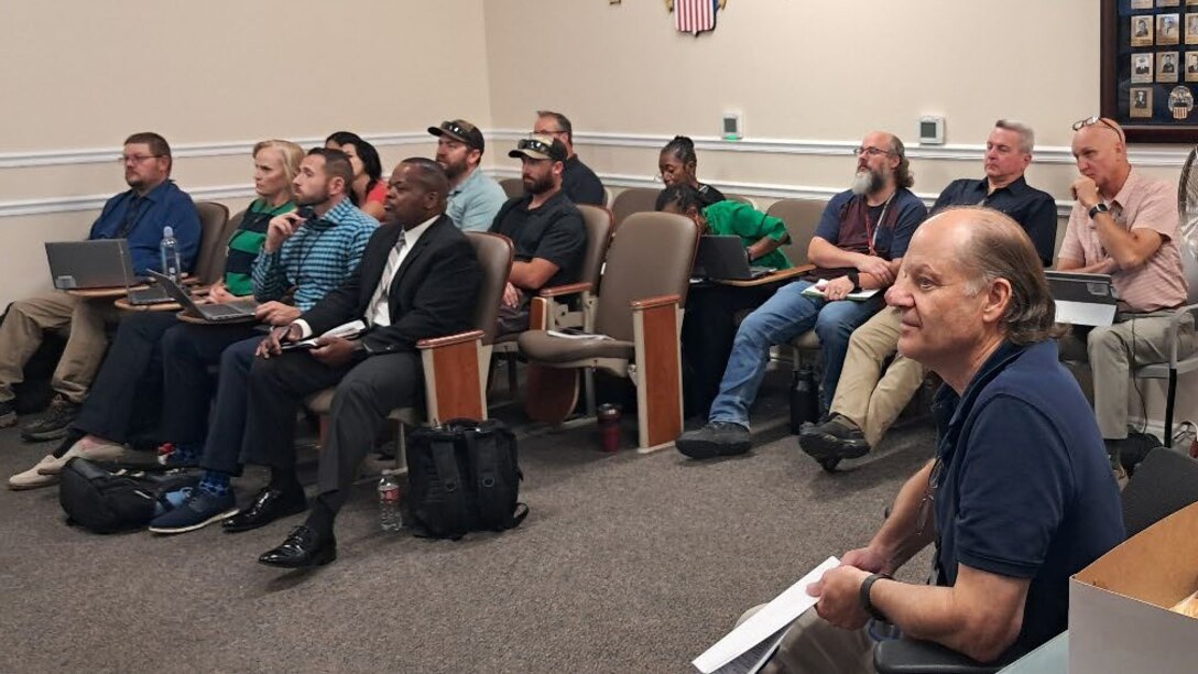 A group of employees sit in a small room looking at a presentation.