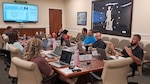 A group of employees sit around a conference table discussing content on a powerpoint slide.
