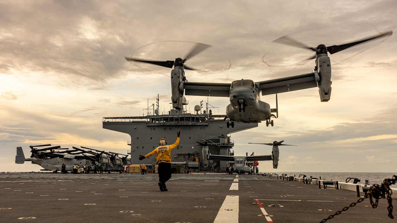 U.S. Navy Petty Officer Second Class Austin Washington, an aviation boatswain mate handler, directs an MV-22B Osprey assigned to Marine Medium Tiltrotor Squadron (VMM) 363, Marine Rotational Force – Darwin 25.3, for landing aboard the expeditionary sea base USS Miguel Keith (ESB 5) in the Philippine Sea, Aug. 29, 2025. For the first time in the rotation’s history, the MRF-D Marine Air-Ground Task Force's Aviation and Ground Combat Elements embarked aboard a U.S. Navy vessel to extend operational reach and provide flexible, combat-credible options across the Indo-Pacific. MRF-D is an annual six-month rotational deployment to enhance interoperability with the Australian Defence Force and allies and partners and provide a forward postured crisis response force in the Indo-Pacific. Washington is a native of California. (U.S. Marine Corps photo by Cpl. Angelina Sara)