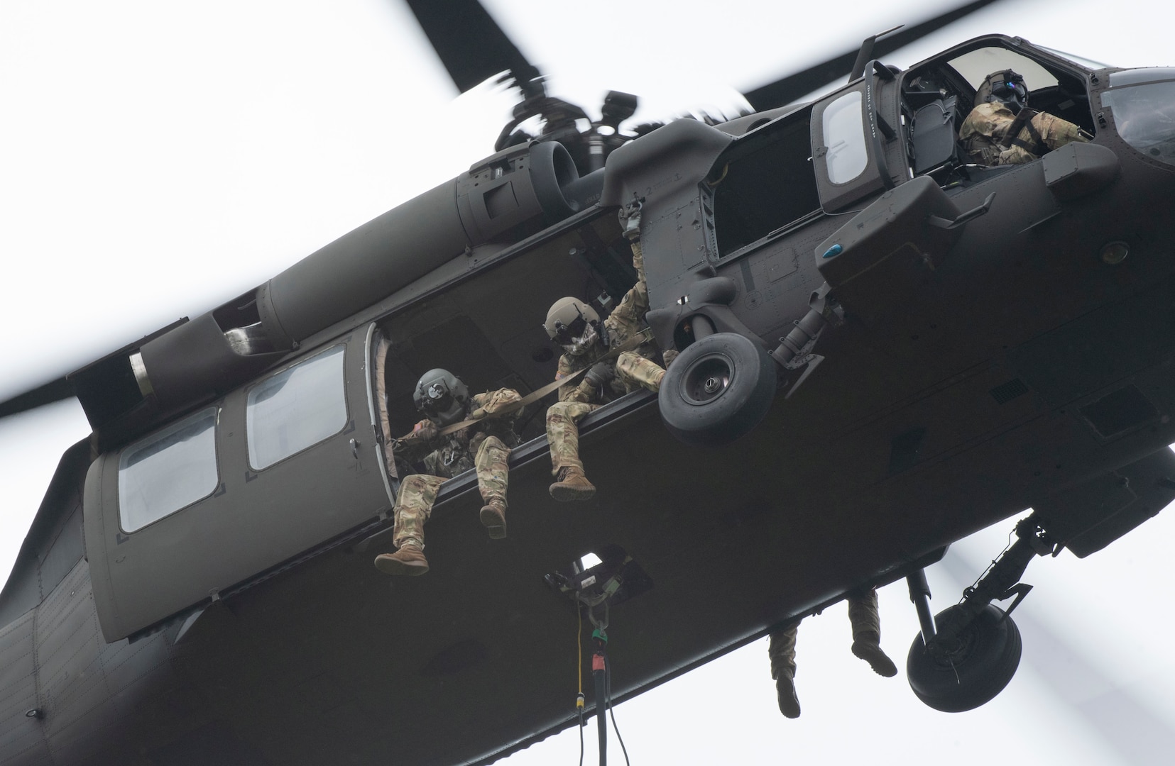 Aviators sit on edge of Black Hawk floor, looking down at their water bucket target