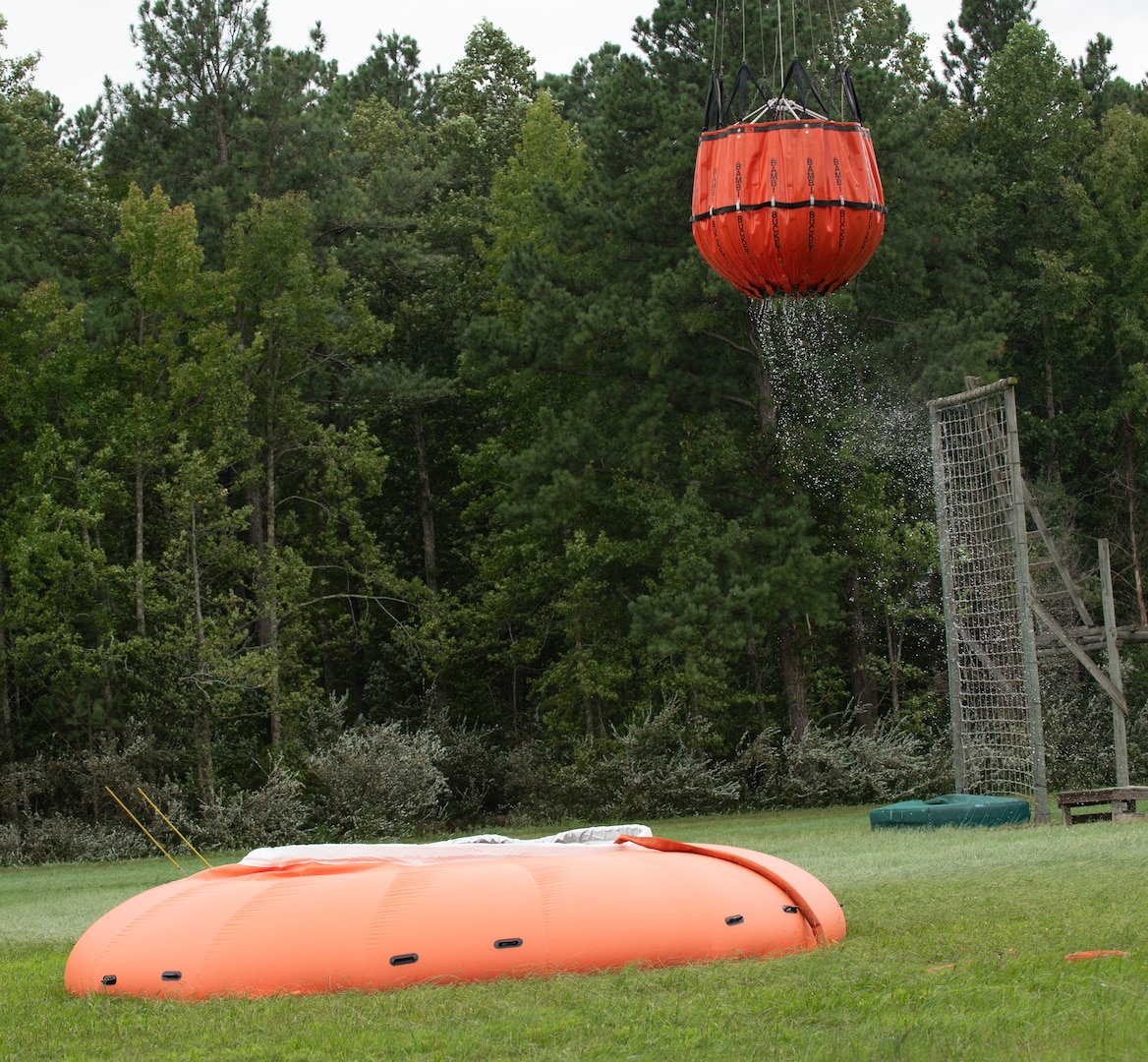 Water bucket dangles from Black Hawk helicopter after retrieving water from portable tank