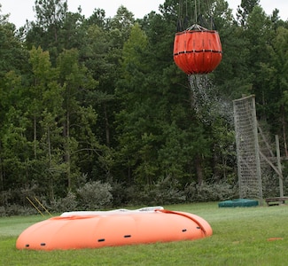Water bucket dangles from Black Hawk helicopter after retrieving water from portable tank