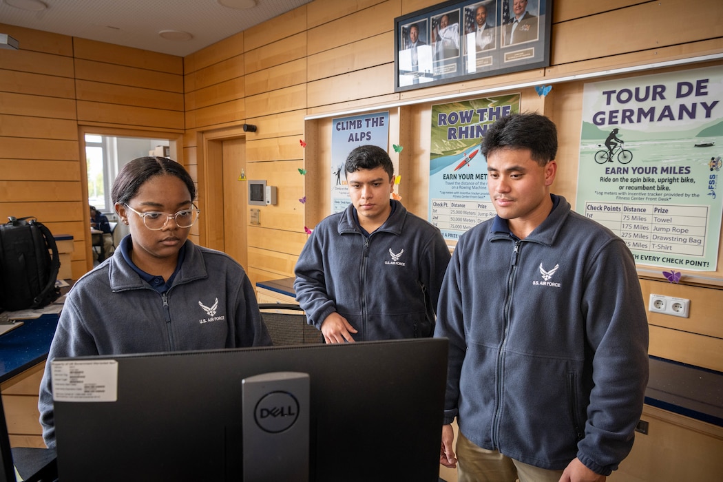 Three Airmen look at a computer monitor