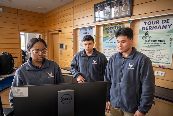 Three Airmen look at a computer monitor