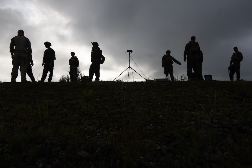 A silhouette of people standing on top of a hill with equipment around them is shown.