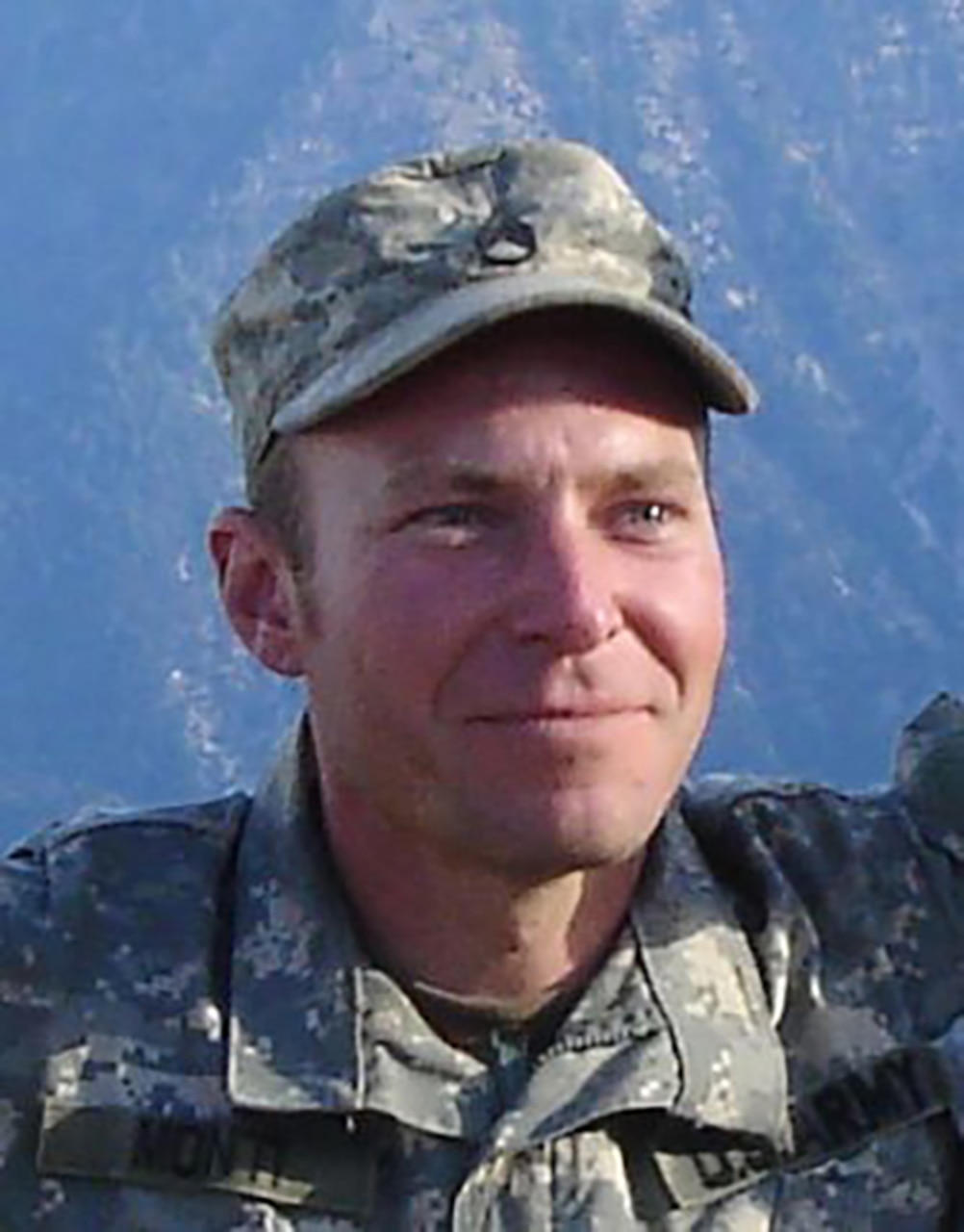 A man in a military camouflage uniform smiles for a photo.