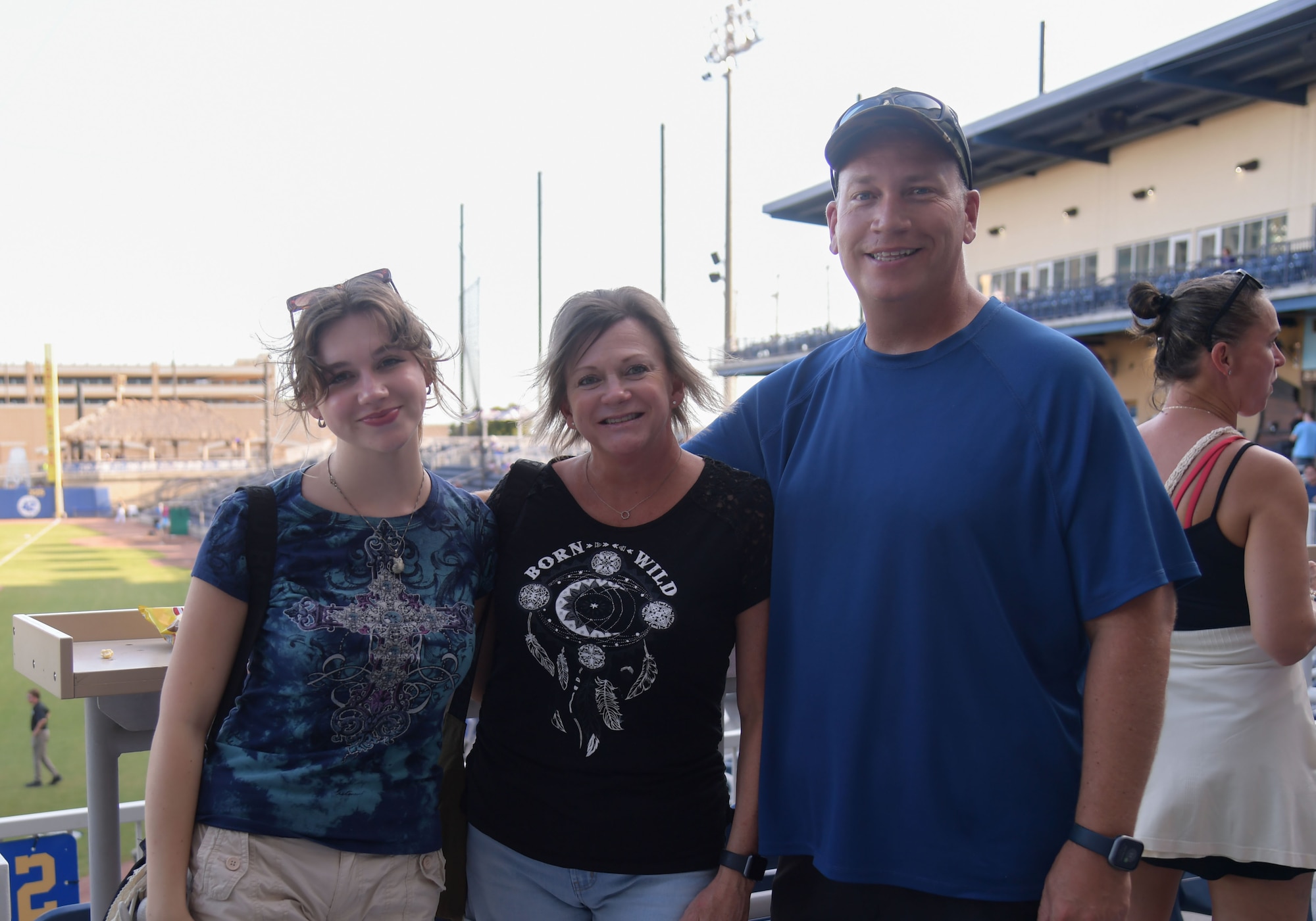 A group of people pose for a photo with a baseball field in the background.