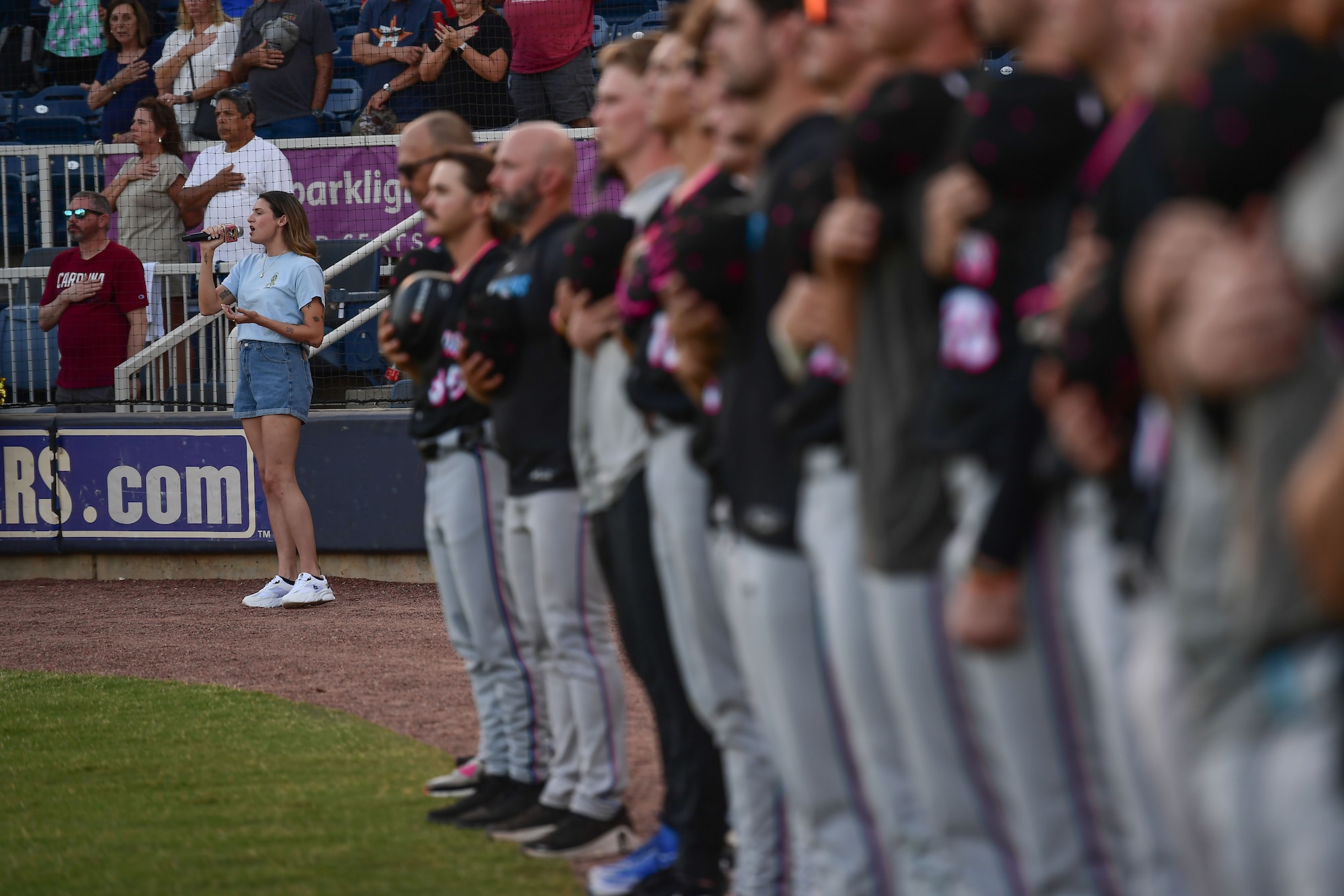 A female sings into a microphone next to a line of baseball players.