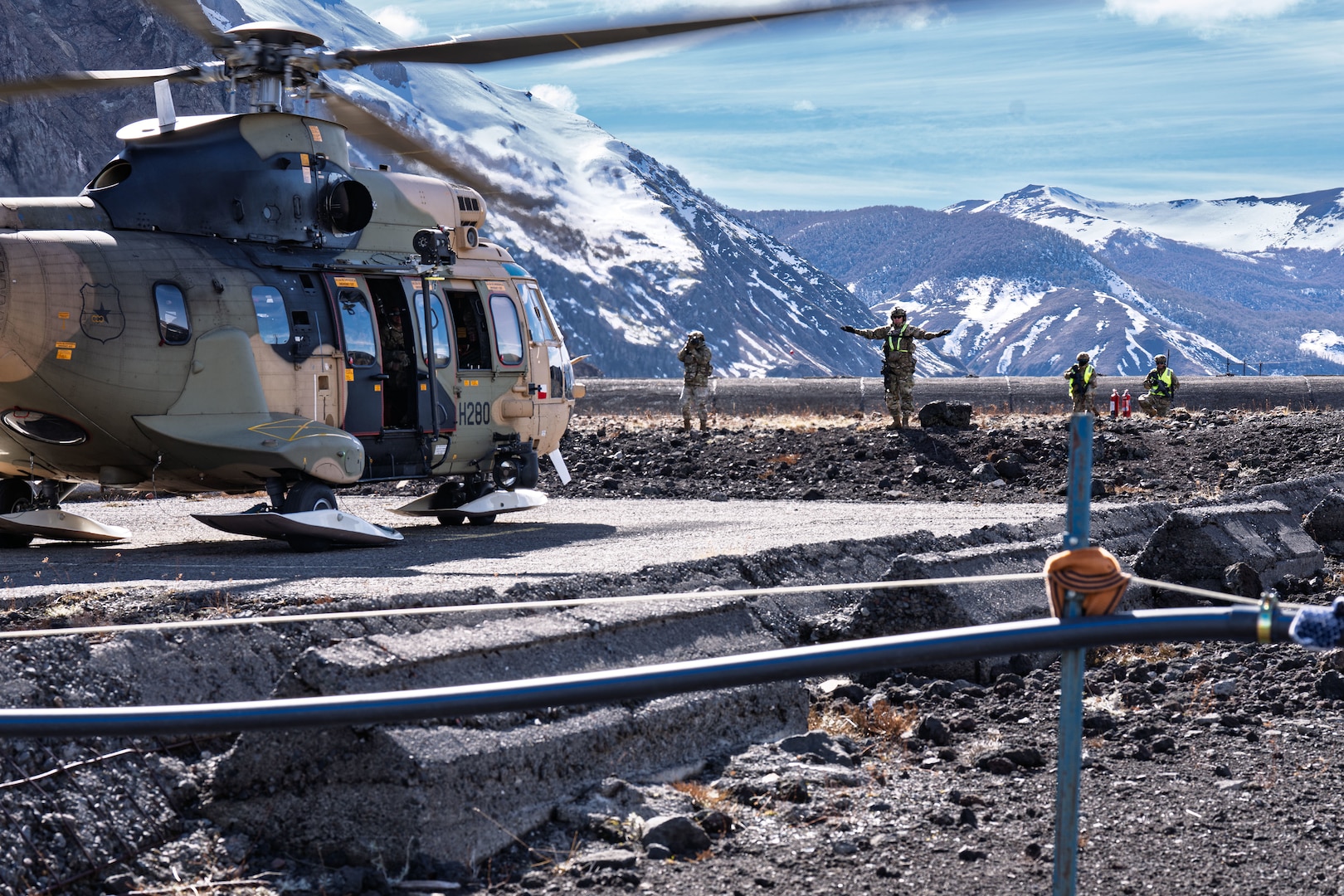 A military helicopter sits on a landing pad in the mountains.