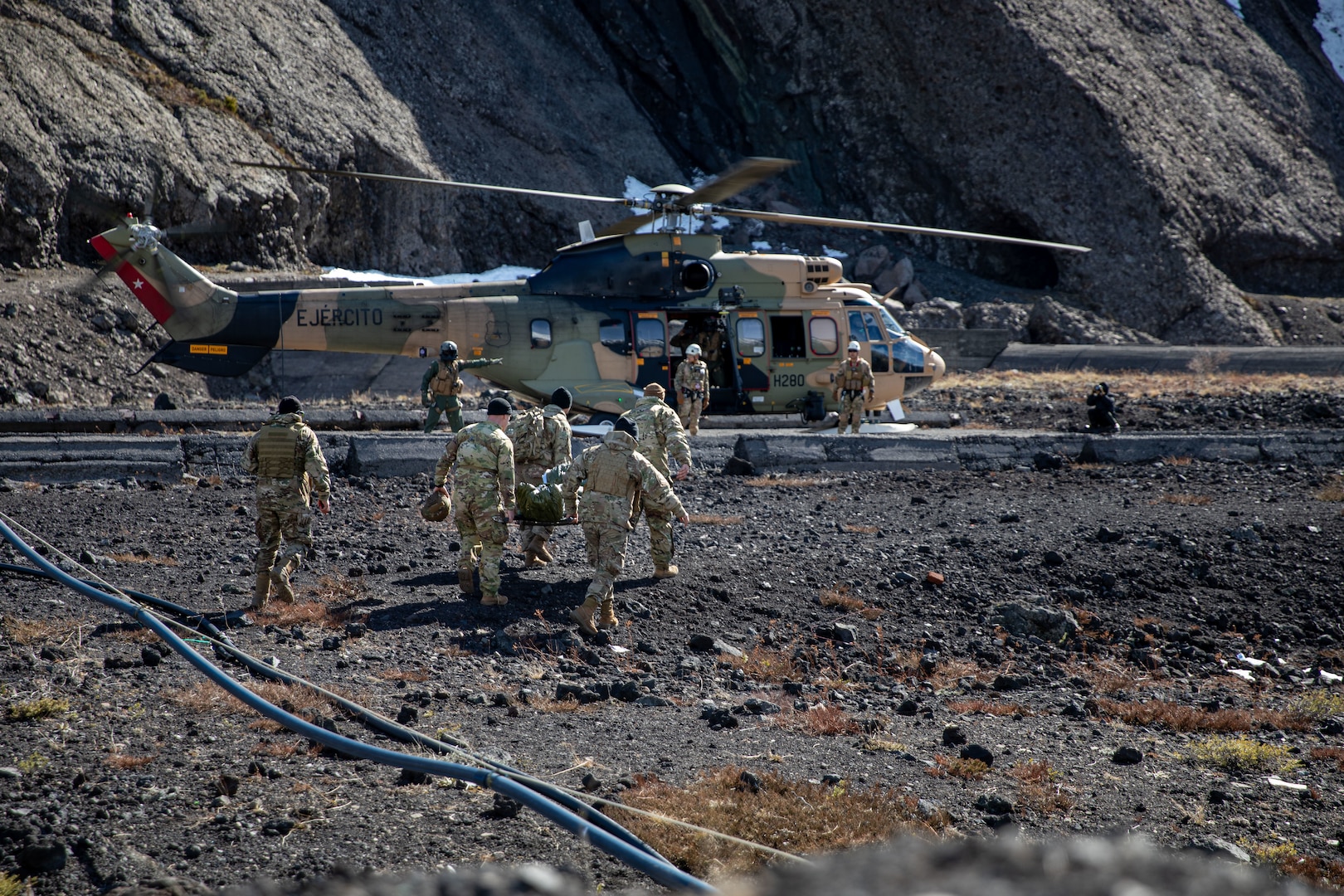 Military personnel in camouflage uniforms carry supplies to a military helicopter