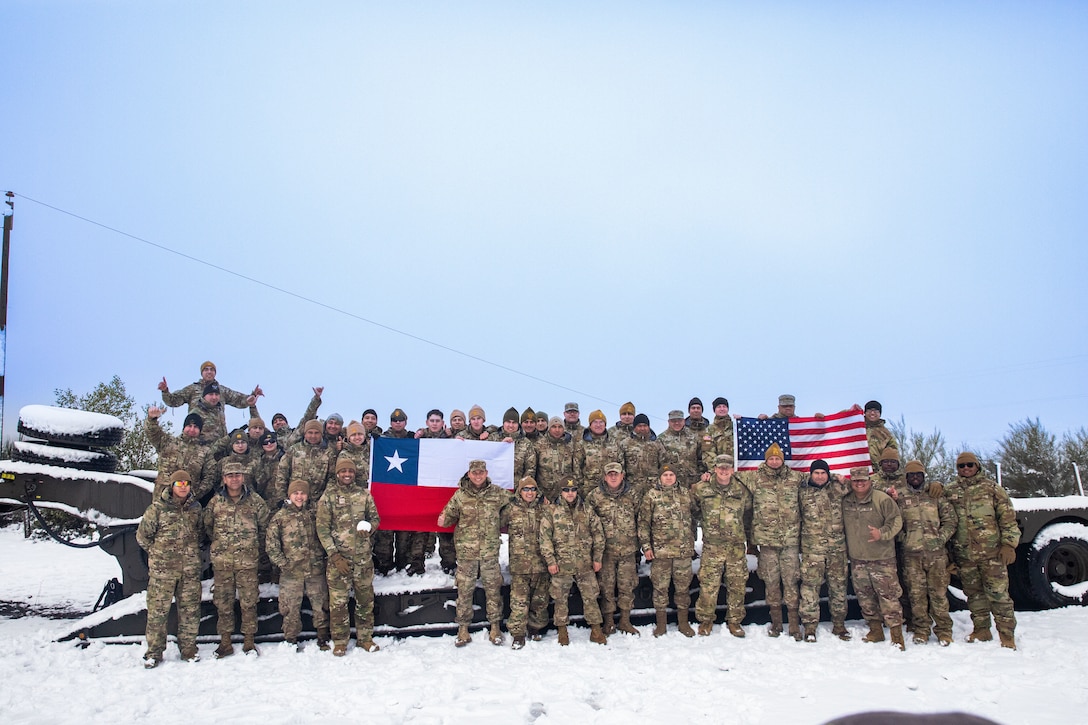 A large group of military personnel in camouflage uniforms pose for a photo while displaying the Chilean and U.S. flags.