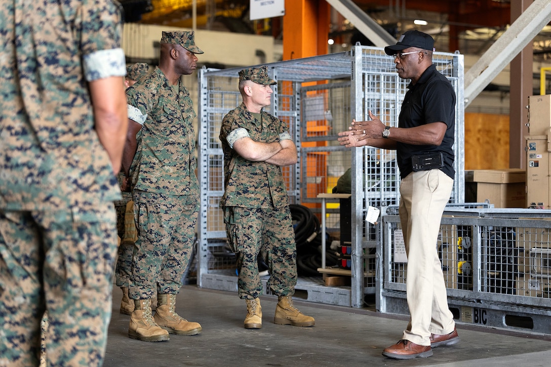U.S. Marine Corps Sgt. Maj. Wesley O. Turner II, senior enlisted leader of Marine Corps Installations East and Marine Corps Base Camp Lejeune, and Brig. Gen. Ralph J. Rizzo Jr., commanding general of MCIEAST-MCB Camp Lejeune, listen to Thurman Bobbett, head of maintenance management at Blount Island Command, Sept. 9, 2025, during the Marine Corps Installations East fall commander’s conference at Marine Corps Support Facility Blount Island in Jacksonville, Florida. Bobbett oversees corrective and preventative maintenance procedures that keep prepositioned Marine Corps equipment combat-ready for global deployment. (U.S. Marine Corps photo by Dustin Senger)