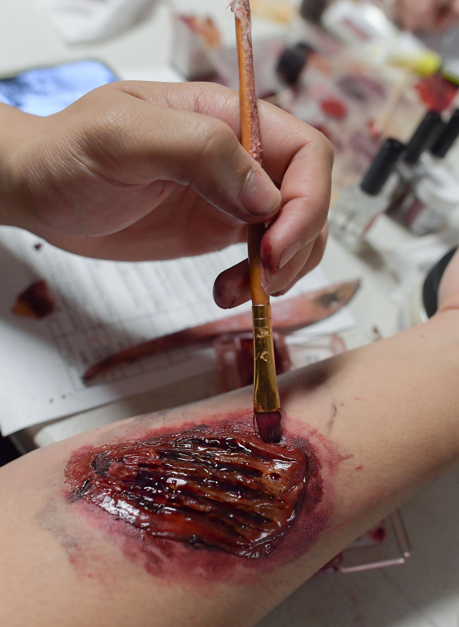 A hand holding a paint brush applies moulage to an arm.