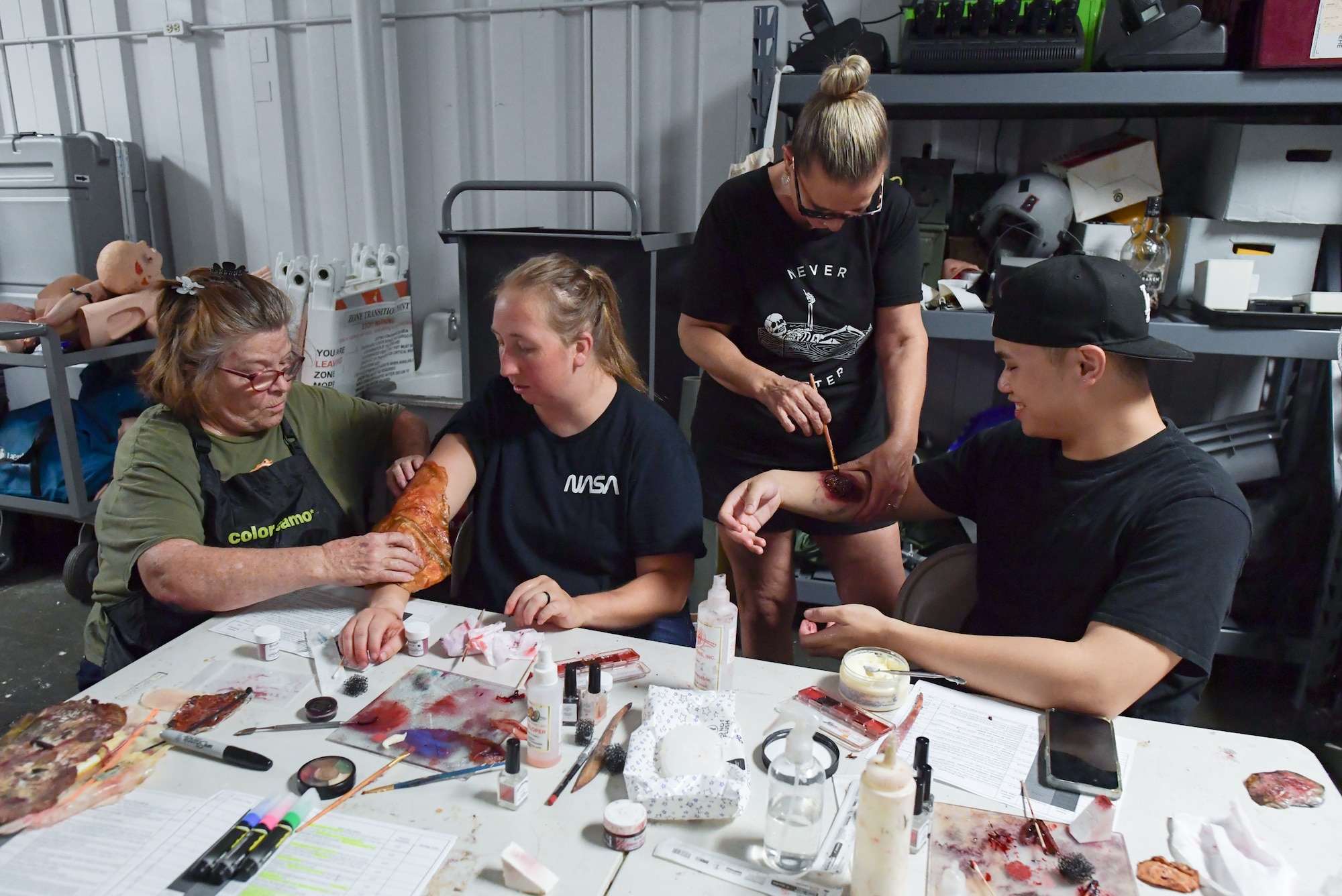 A group of people sit around a table while applying moulage to themselves.