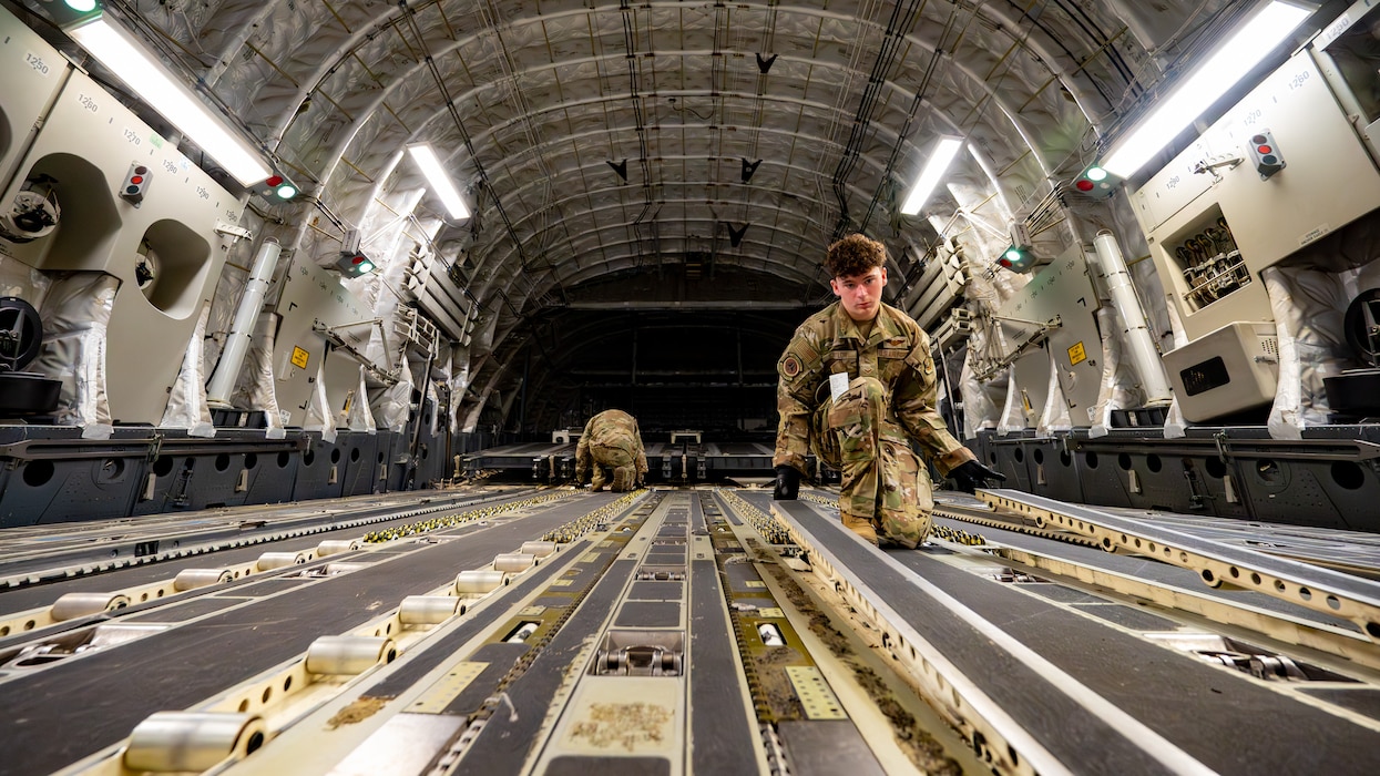 Airmen kneel to swap rails inside a C-17 cargo bay