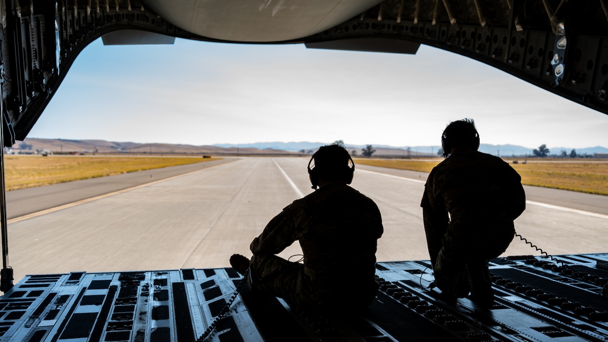 Two Airmen sit at the back open door of a C-17