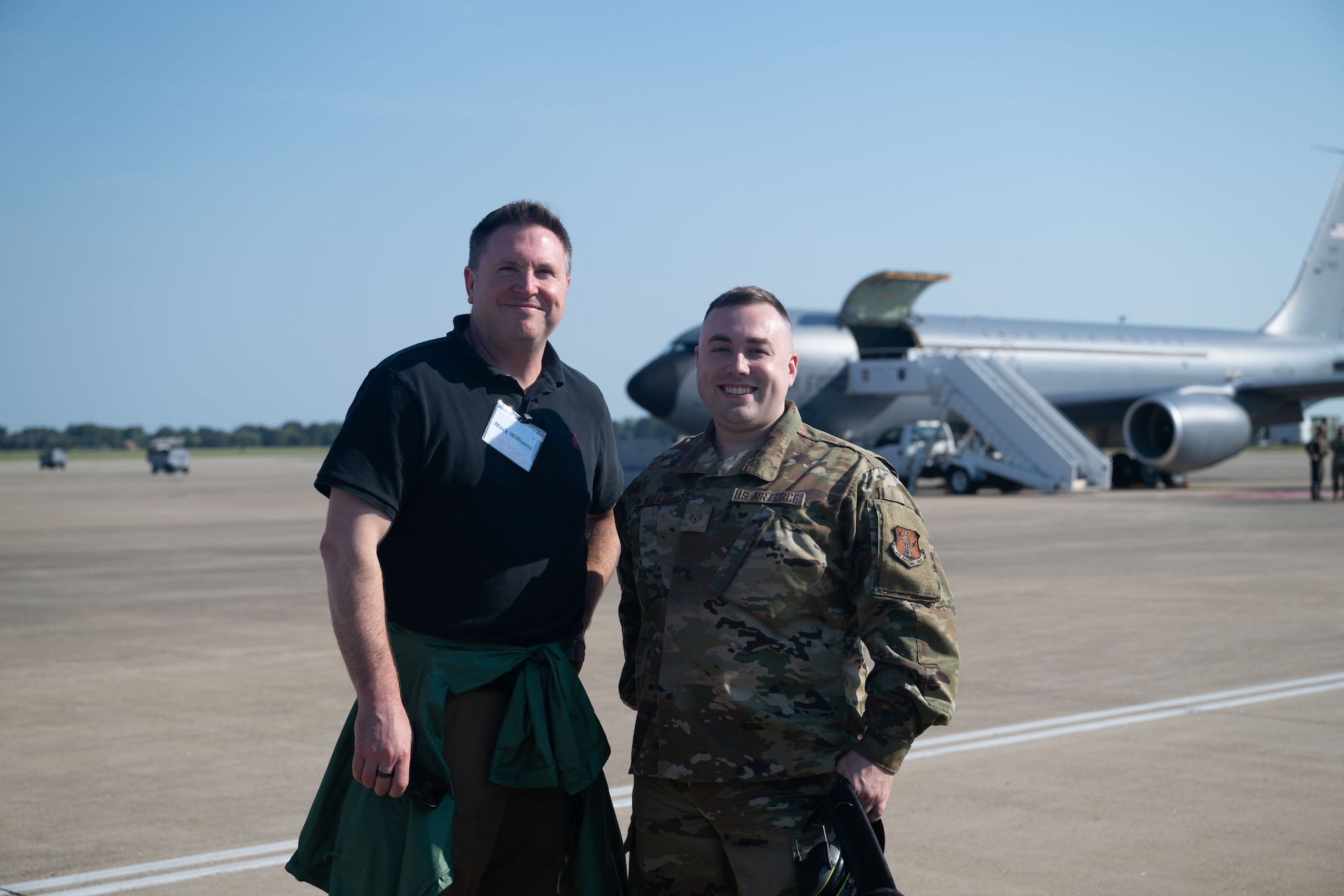 An Airman, right, stands with his civilian employer on the flightline with a KC-135 in the background