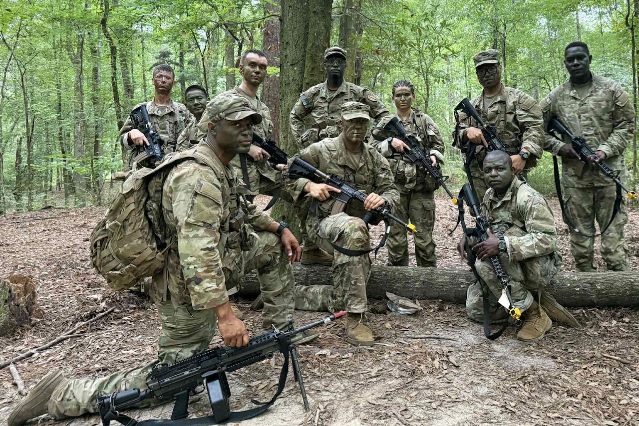 Soldiers in camouflage uniforms with guns mill about in the forest.