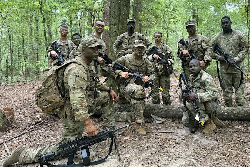 Soldiers in camouflage uniforms with guns mill about in the forest.