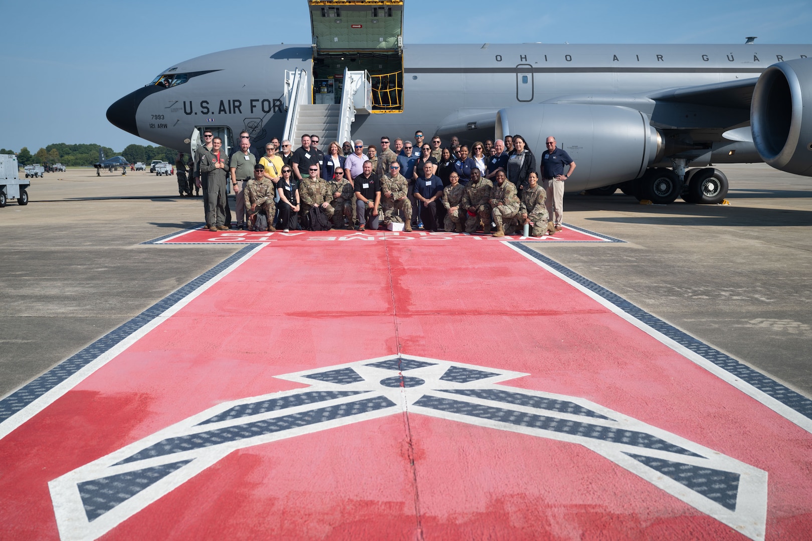 Group of civilian employers and military personnel posing for a group photo with a red walkway and Air Force symbol, KC-135 in the background
