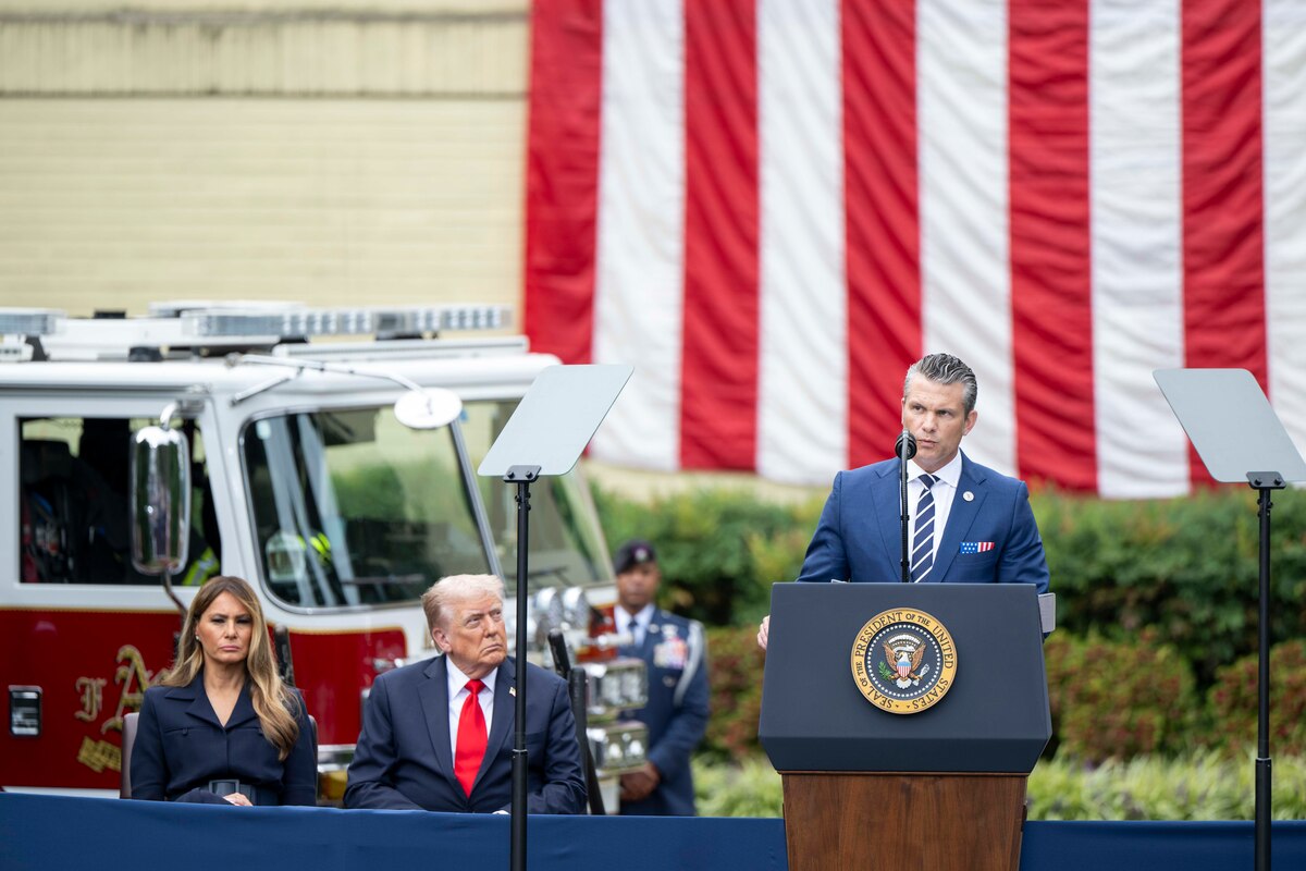 The secretary of war speaks at a podium as the president and first lady watch from the left.