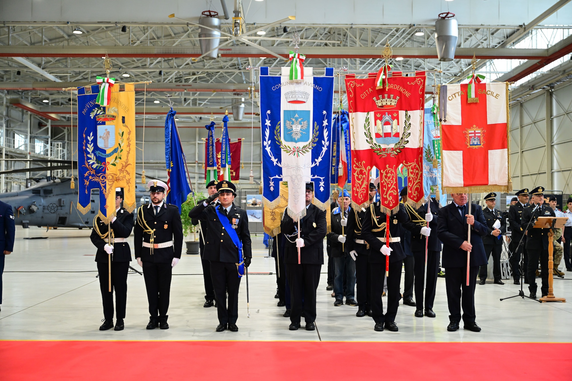 Italian Air Force veterans stand in formation holding up various flags.