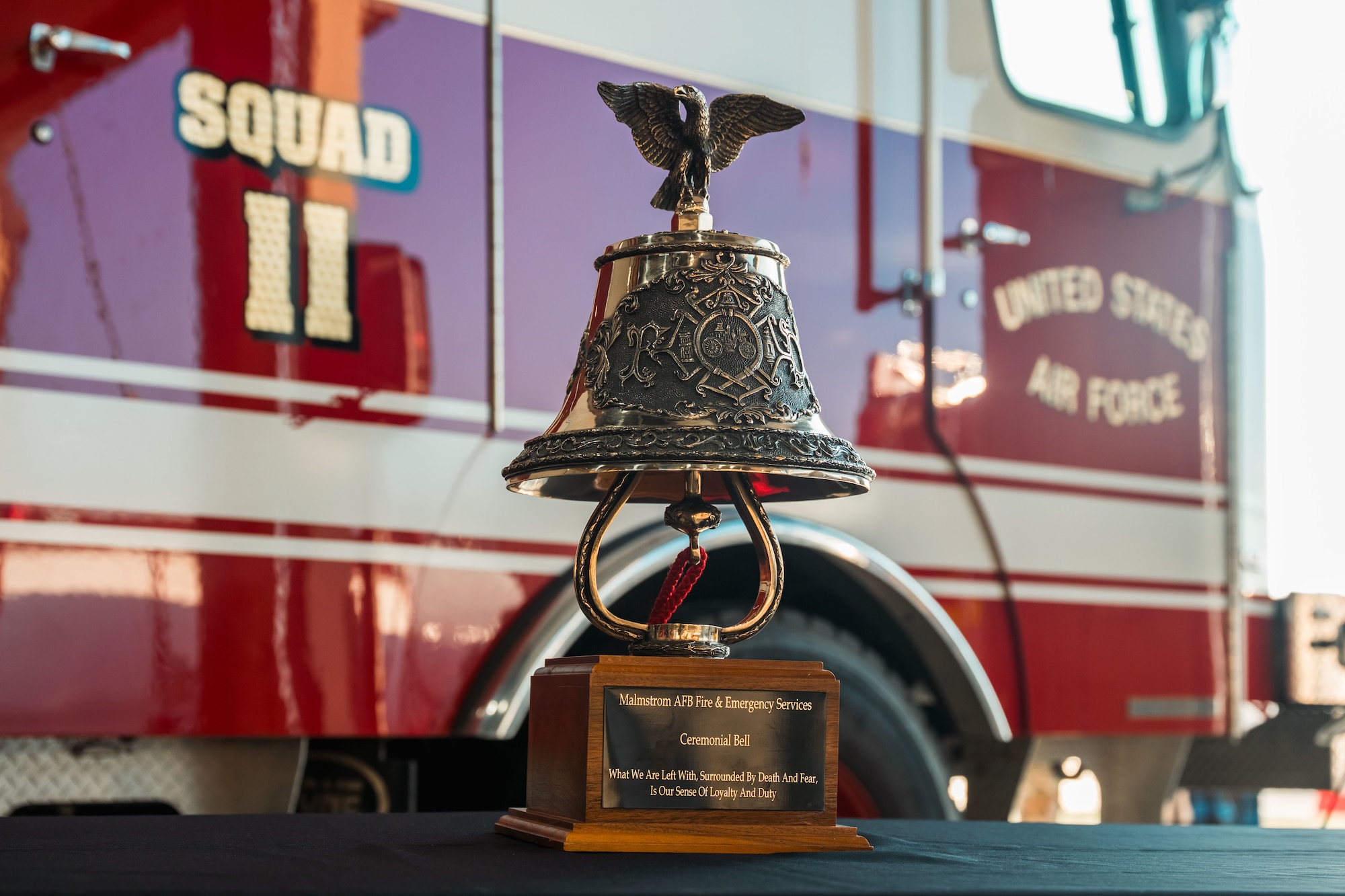 A ceremonial bell is displayed on a table with a firetruck in the background.