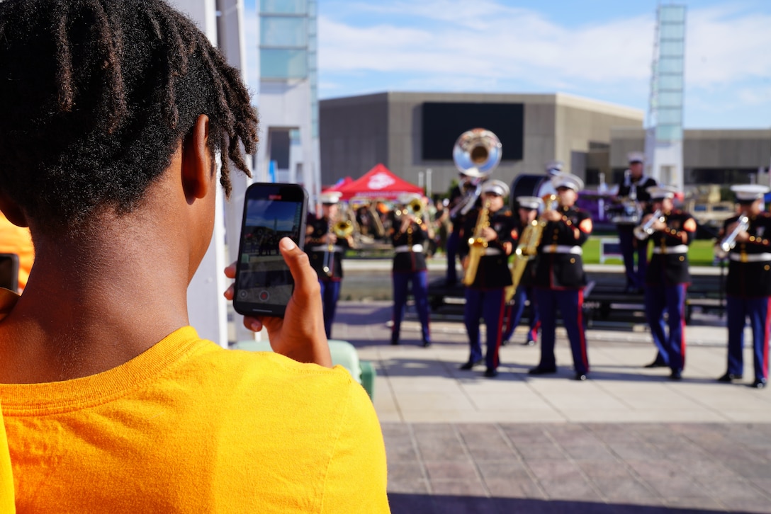 Civilian photographs the 2nd Marine Aircraft Wing Band, brass band, assigned to Special Purpose Marine Air-Ground Task Force-250 as they perform at the static display during Marine Week Atlanta, Aug. 30, 2025. Marines stationed across the globe commemorate the 250th anniversary of the Marine Corps, honoring a distinguished legacy of service, sacrifice, and unwavering fidelity to both the nation and the Corps. (U.S. Marine Corps photo by Staff Sgt. Matthew Booth)