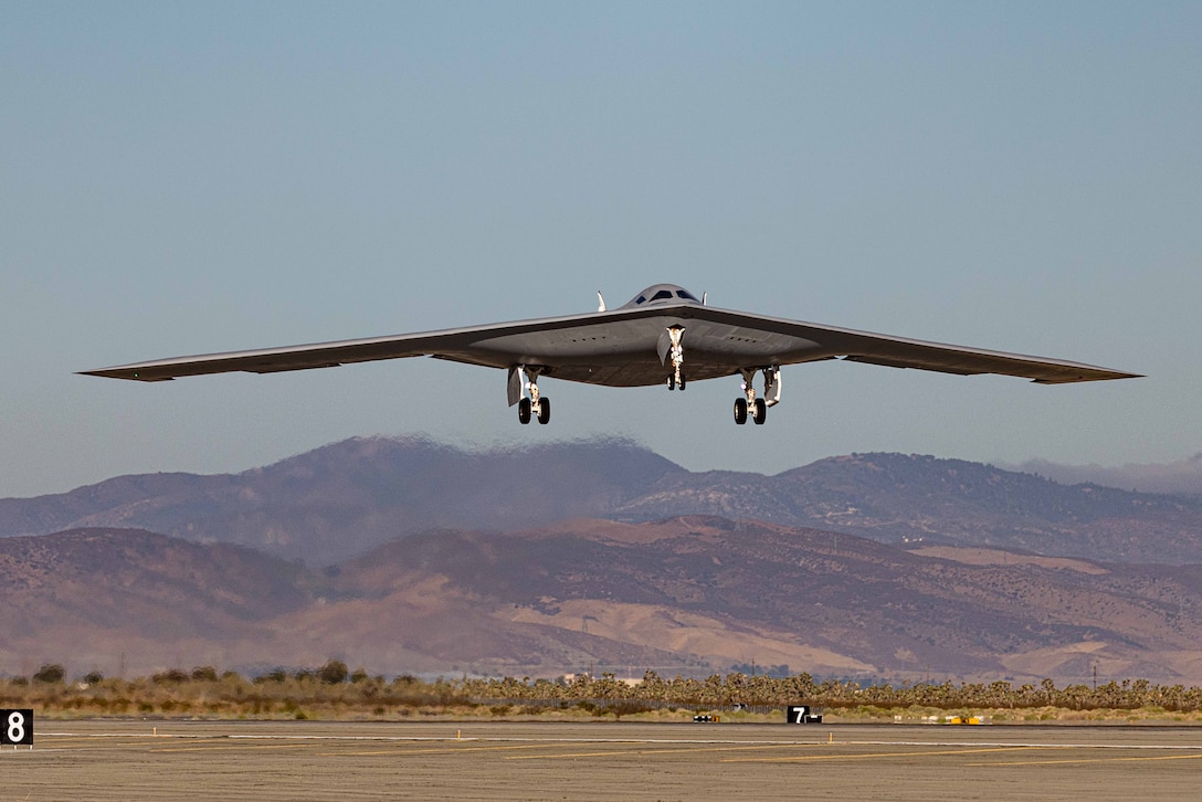 A wide and narrow aircraft takes off from a runway during the day with mountains in the distance, as seen from head on.