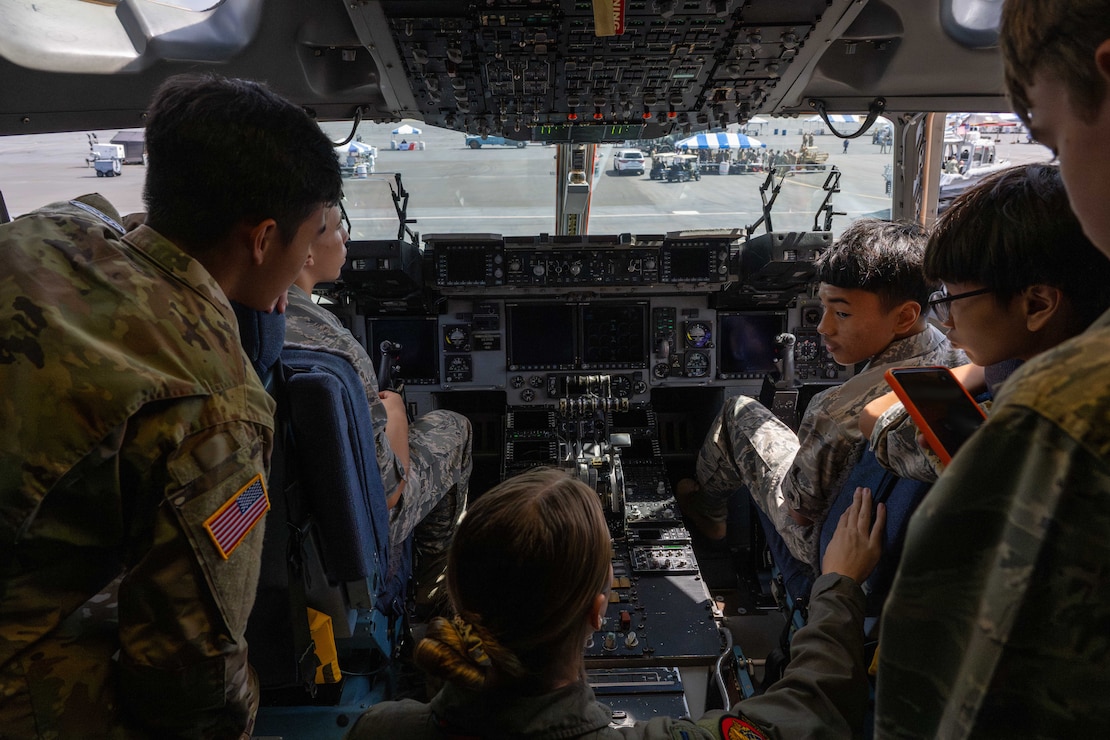 U.S. Air Force Junior Reserve Officer Training Corps cadets sit in the cockpit of a C-17 Globemaster III with a pilot.