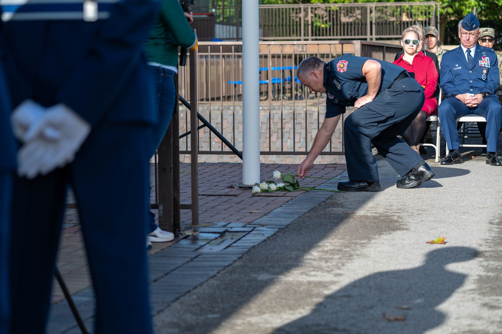 A firefighter places a white rose at the base of the flagpole