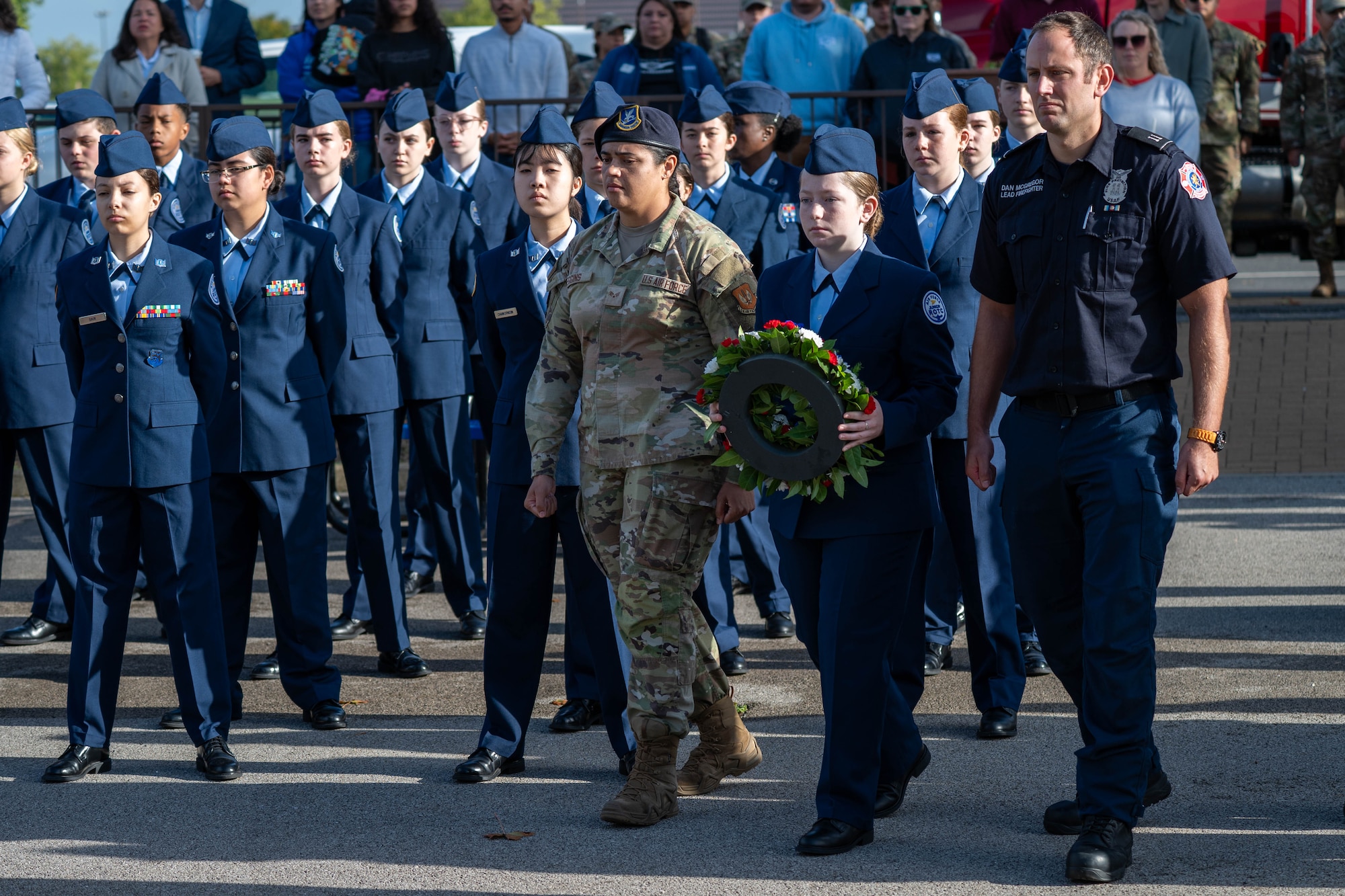 A U.S. Air Force Airman, Junior ROTC cadet, and firefighter carry a wreath during a 9/11 memorial ceremony