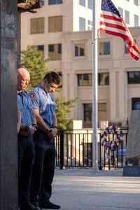 Firefighters from the Indianapolis Fire Department’s Station 13 take part in a moment of silence during a commemoration ceremony at the Indiana 9/11 Memorial in Indianapolis Sept. 11, 2025. Standing between the firefighters and the flag was a beam from one of the towers at the World Trade Center, which was destroyed by the terrorist attacks on Sept. 11, 2001. (U.S. Army photo by Mark R. W. Orders-Woempner)