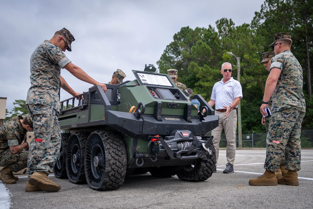 Lewis Martin, a sales consultant and support representative with Hunter Defense Technologies Global, center right, speaks to U.S. Marines with 2nd Distribution Support Battalion, Combat Logistics Regiment 2, 2nd Marine Logistics Group, about the applications of a Hunter WOLF unmanned ground vehicle during a delivery from Naval Surface Warfare Center, Marine Corps Warfighting Lab, to 2nd DSB at Marine Corps Base Camp Lejeune, North Carolina, Sept. 9, 2025. 2nd DSB received these UGVs as part of a partnership with MCWL to test and evaluate their capabilities, exploring new operational concepts and assessing their potential to augment logistics and enhance overall combat readiness. (U.S. Marine Corps photo by Sgt. Alfonso Livrieri)