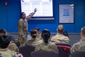 U.S. Air Force Tech. Sgt. Imani Williams, 375th Force Support Squadron fitness and sports operations manager, points to a large screen displaying a physical fitness assessment score chart when instructing a class of augmentees at Scott AFB.