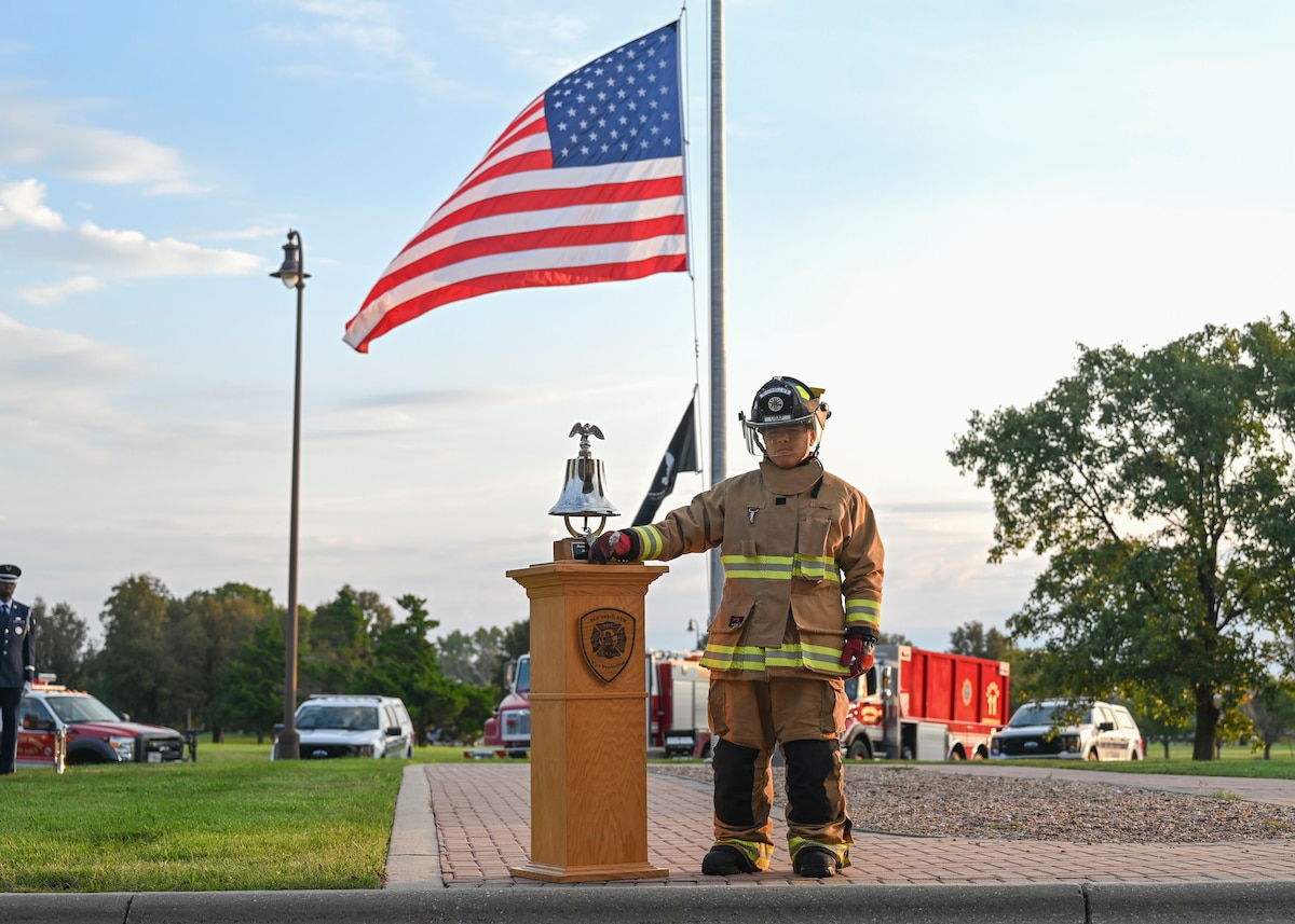 A man in fire fighter bunker gear rings a silver bell.