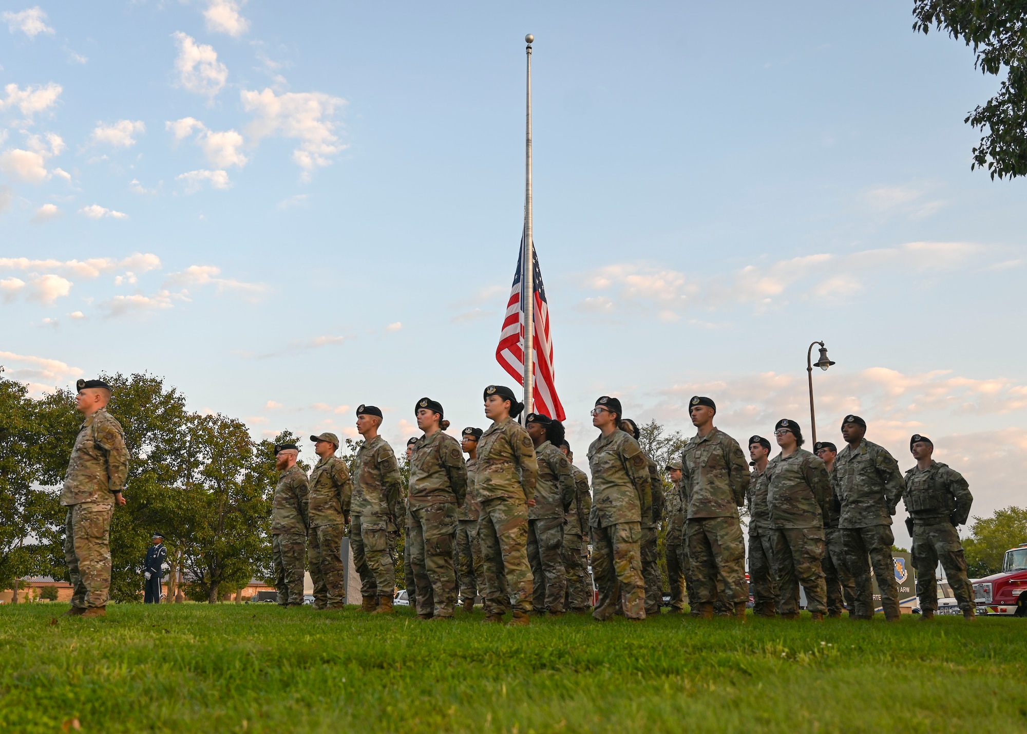 A group of people in military uniforms stand in lines next to a flagpole with an American flag on it.