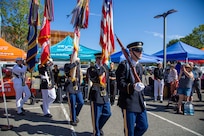 Military members carrying flags and rifles are marching during an outdoor ceremony.