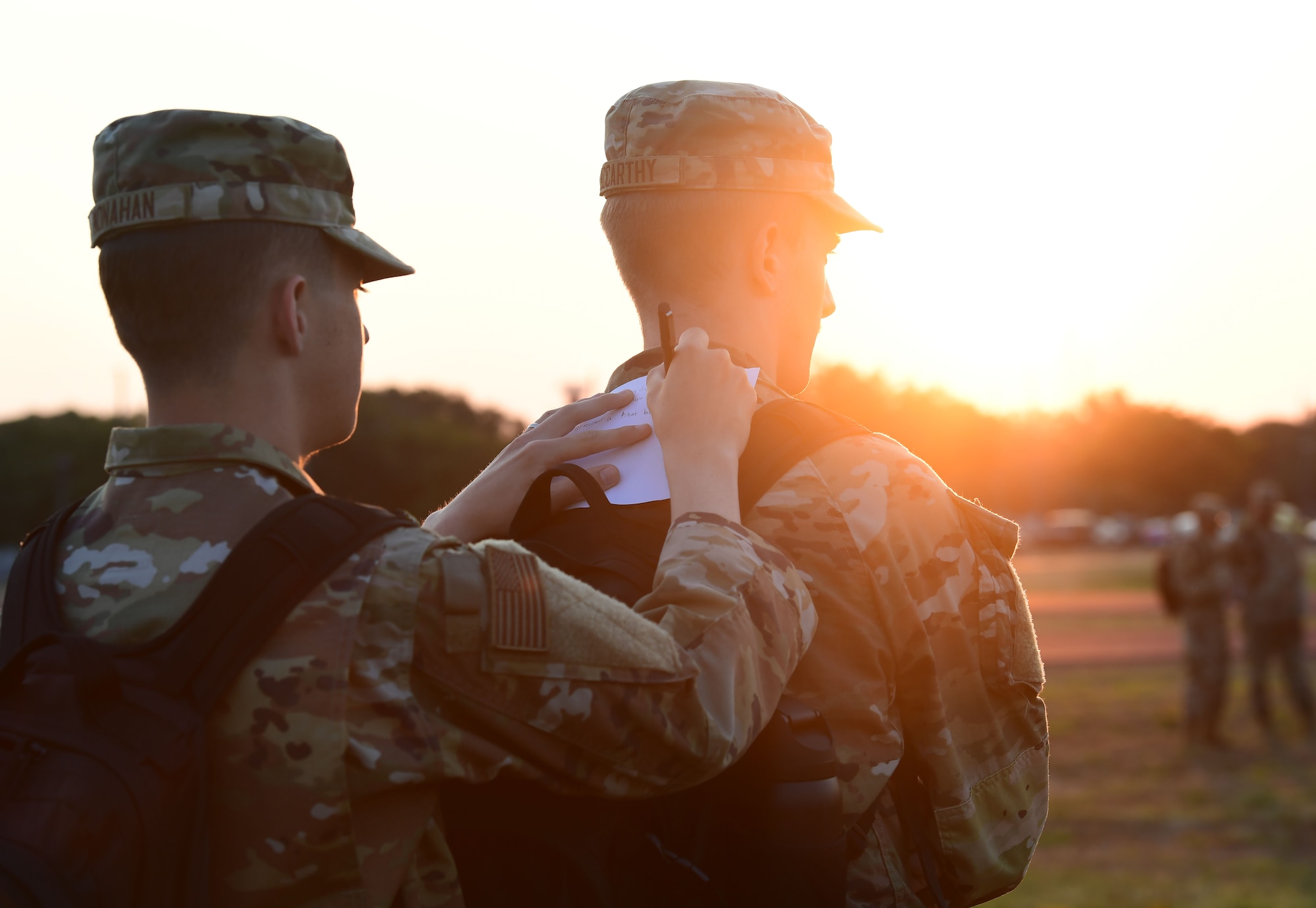 A man in military uniform writes on a piece of paper using the back of another man in military uniform.
