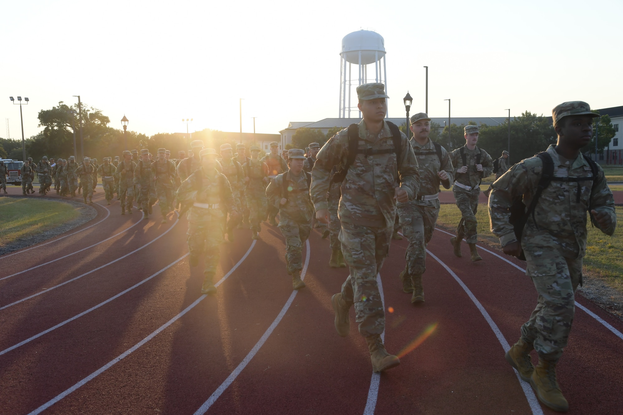 A group of people in military uniform run across a running track.