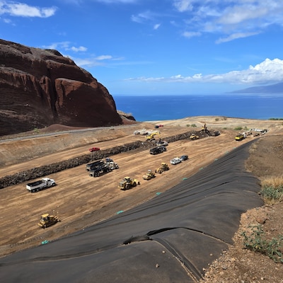 Trucks moving on a dirt path with the ocean in the background