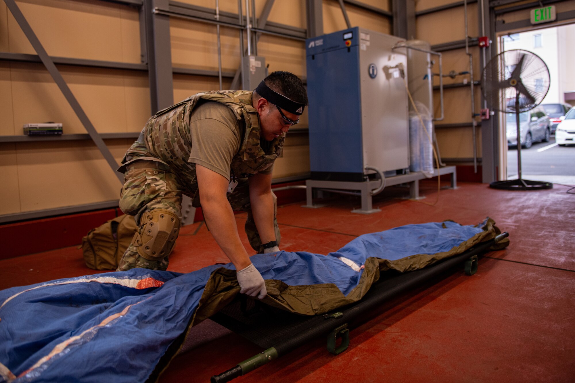 An Airman crouches as they spread a blue tarp over a stretcher.