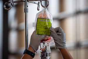 A pair of hands wearing grey gloves writes on the label of an empty blood bag.