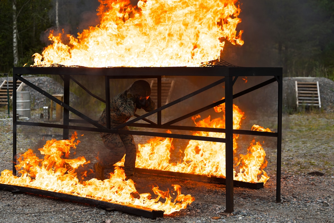 U.S. Marine Corps Chemical. Biological, Radiological, and Nuclear specialists with 2d Light Armored Reconnaissance Battalion, 2d Marine Division, pass through an obstacle surrounded by burning napalm during a fire safety class taught by Swedish allies at Berga Naval Base, Sweden, Aug. 28, 2025. The training served to enhance the relationship between the United States and Sweden, improving joint readiness and interoperability between NATO partners. (U.S. Marine Corps photo by Cpl. Xavier Alicea)